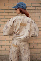 Person wearing a beige coverall with celestial pattern against a brick wall.