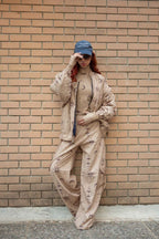 Person wearing a beige patterned outfit and blue cap against a brick wall.