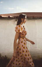 Woman wearing a patterned skirt standing against a white wall with a red-tiled roof.