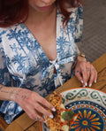 Person in a blue and white patterned outfit with tattoos, holding a slice of pizza over a colorful plate.