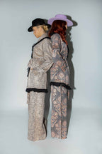 Two people wearing patterned outfits with hats against a plain background