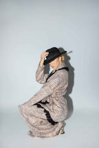 Person wearing a long patterned dress and black hat on a light gray background
