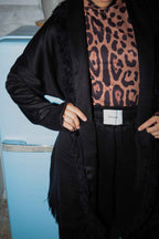 Person wearing a black coat with a leopard print top in front of a blue refrigerator.