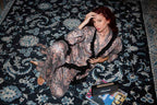 Woman in a patterned robe sitting on a decorative rug with a Gucci wallet and magazine.
