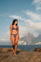 Woman in a bikini standing on a rocky beach with mountains in the background