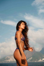 Woman in a bikini standing on a beach with mountains and blue sky in the background