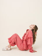 Woman in red checkered outfit sitting on a beige floor with a neutral background