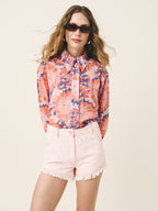 Woman wearing a colorful floral blouse and pink shorts against a plain background