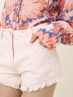Person wearing a colorful floral top and light pink shorts with fringe details.