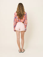Person wearing a colorful tie-dye shirt and pink shorts on a plain background