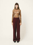 Person wearing a leopard print top and burgundy pants on a white background