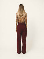 Person wearing a leopard print top and burgundy pants on a white background