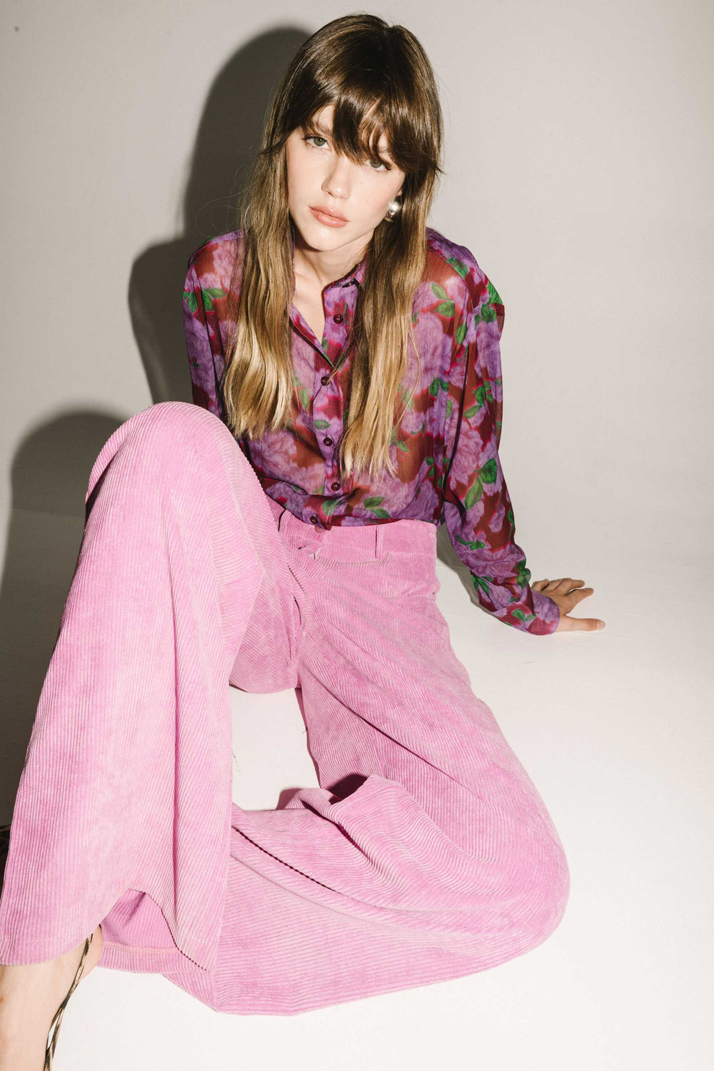 Woman wearing a colorful blouse and pink pants against a white background