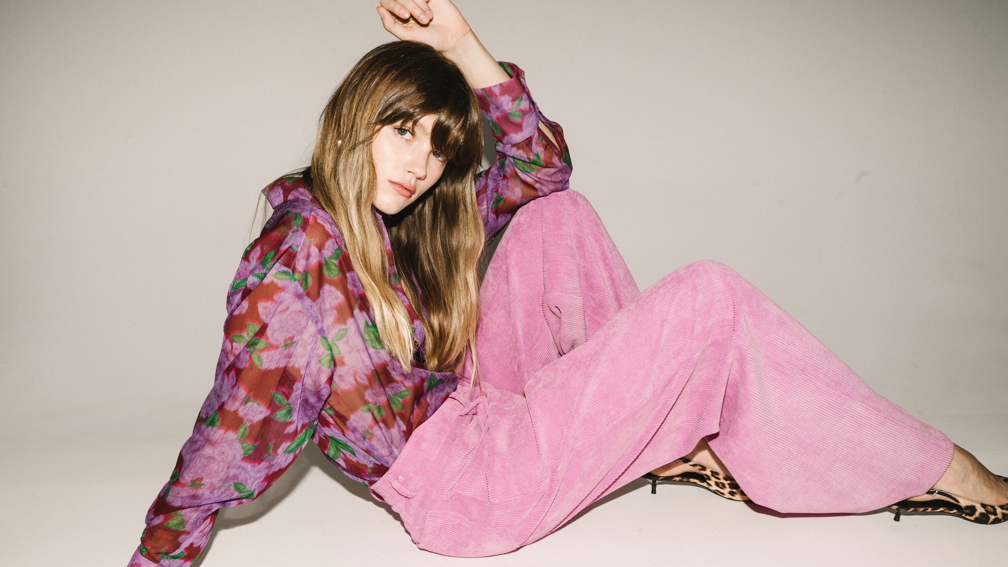 Woman wearing a floral blouse and pink pants sitting on a white floor.