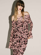Woman wearing a pink and black floral off-shoulder dress against a plain background
