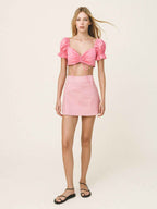 Woman wearing a pink top and skirt set on a plain background
