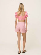 Woman wearing a pink crop top and shorts set on a light beige background