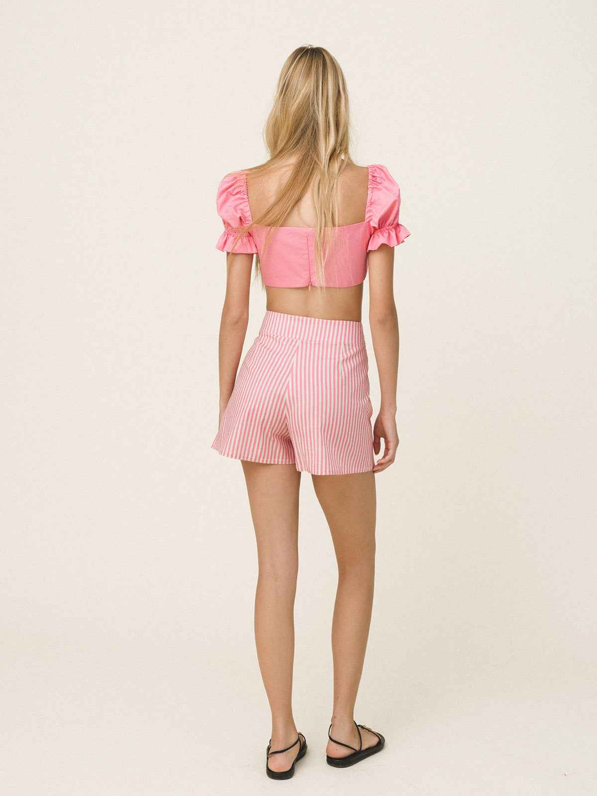 Woman wearing a pink crop top and shorts set on a light beige background