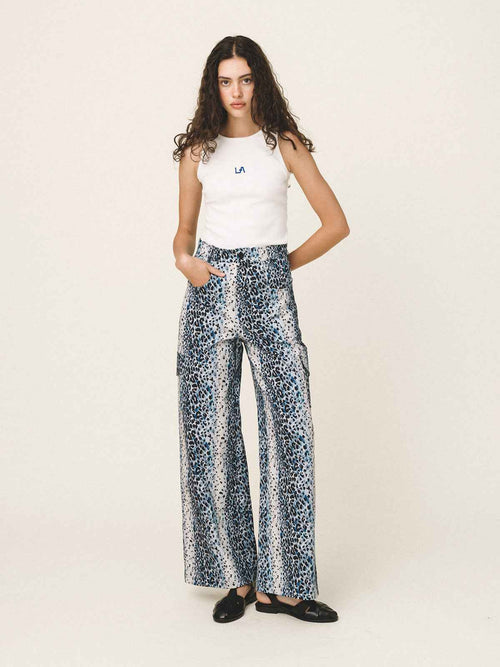 Woman wearing a white sleeveless top and patterned pants on a white background