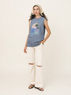Woman wearing a sleeveless graphic shirt and white pants on a plain background