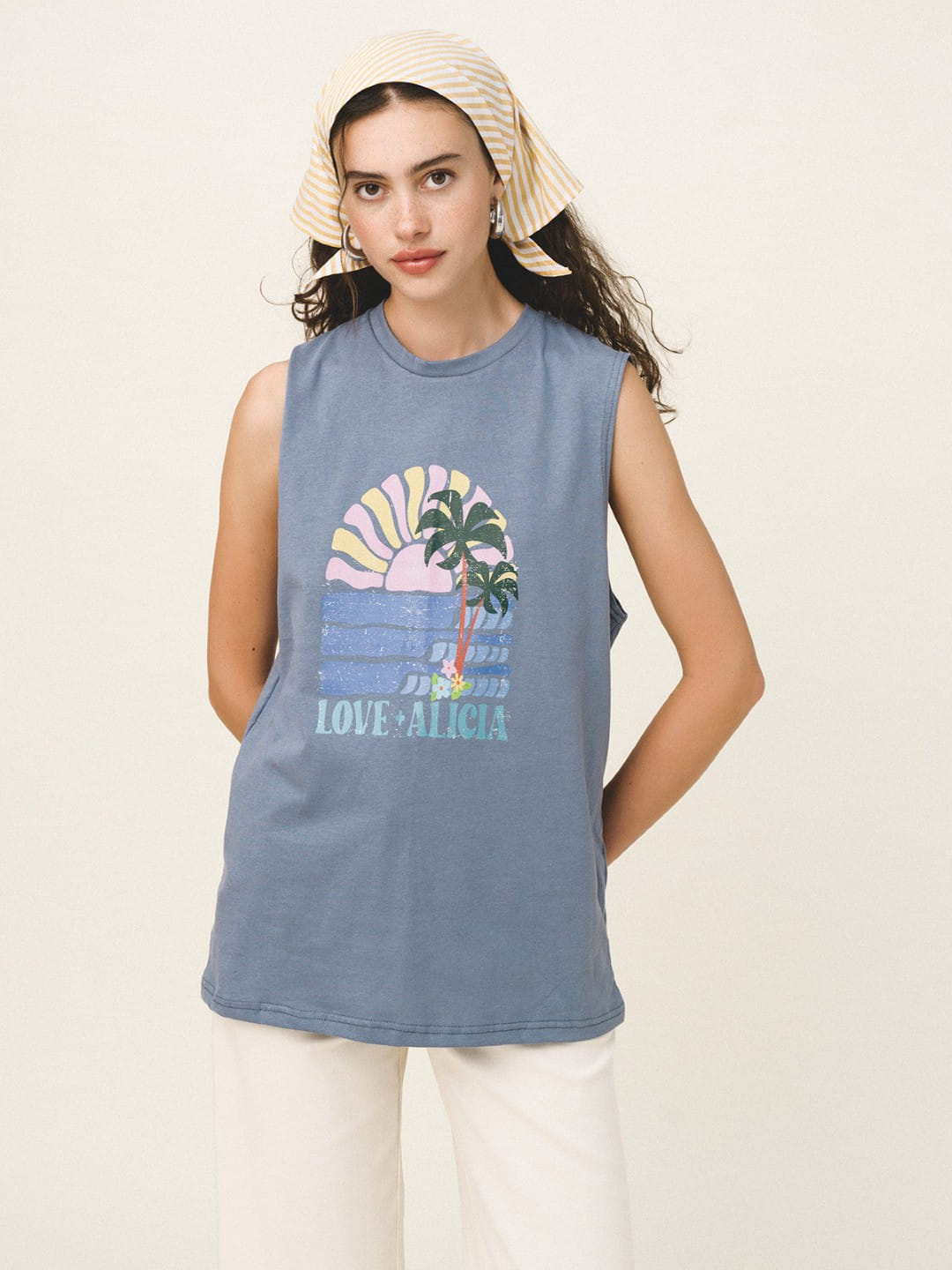 Woman wearing a sleeveless blue shirt with a palm tree and sunset design on a beige background