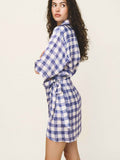 Woman wearing a blue and white checkered dress with a belt on a plain background