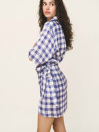 Woman wearing a blue and white checkered dress with a belt on a plain background