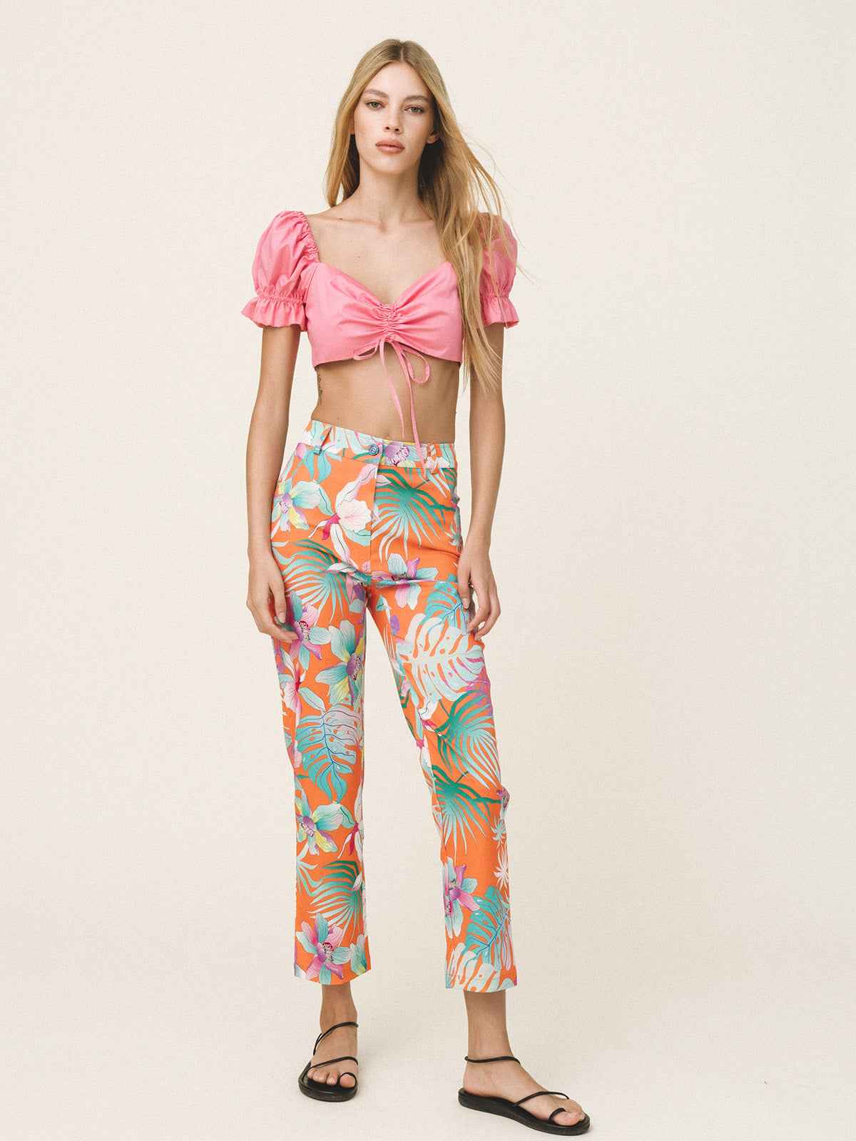Woman wearing a pink top and colorful floral pants on a white background