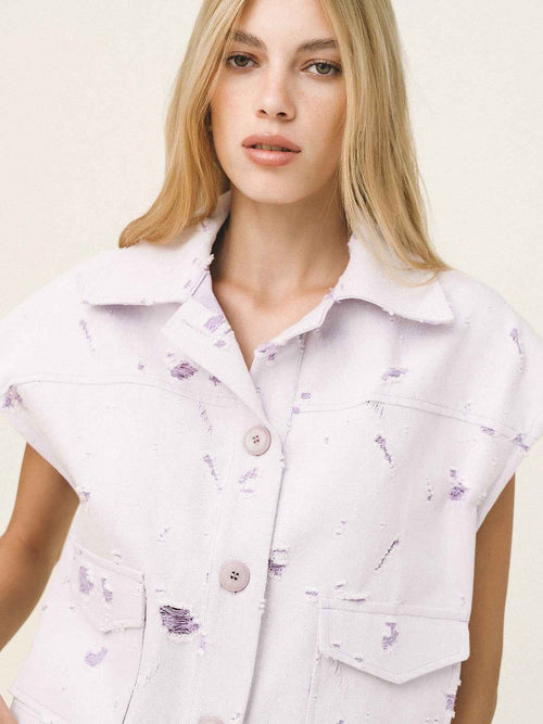 Woman wearing a light purple sleeveless shirt with floral patterns on a plain background
