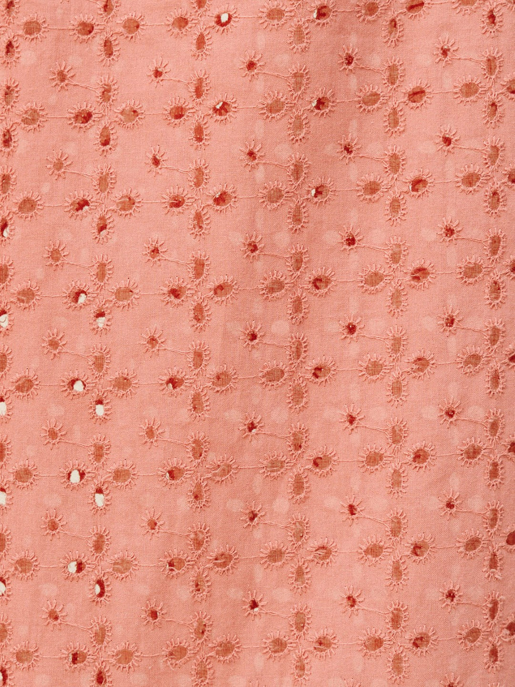A close-up of a peach-colored fabric featuring a repeating pattern of embroidered floral motifs and small metallic silver mirror-work embellishments.