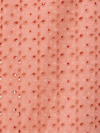 A close-up of a peach-colored fabric featuring a repeating pattern of embroidered floral motifs and small metallic silver mirror-work embellishments.
