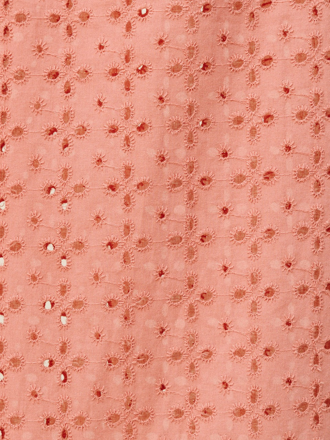 A close-up of a peach-colored fabric featuring a repeating pattern of embroidered floral motifs and small metallic silver mirror-work embellishments.