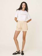 Woman wearing a white t-shirt with text and beige shorts on a plain background