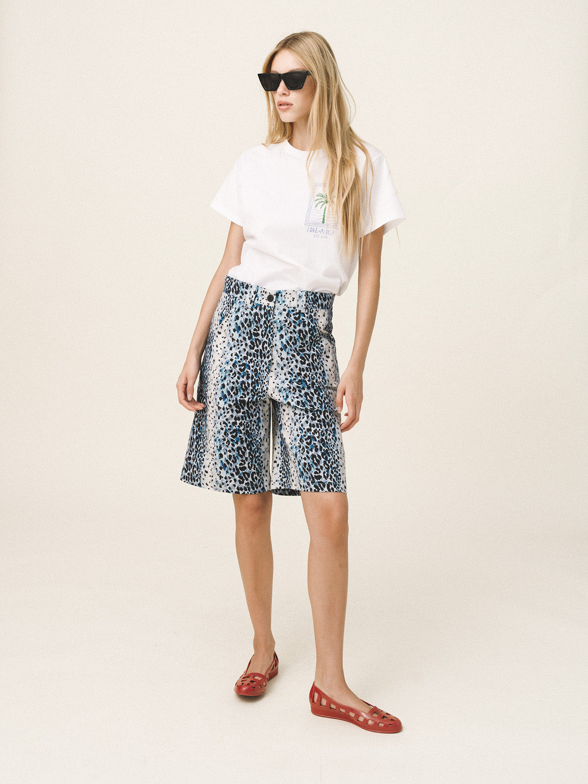 Woman wearing a white t-shirt and floral skirt with red shoes on a white background