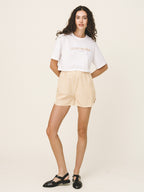 Woman wearing a white t-shirt with text and beige shorts on a plain background