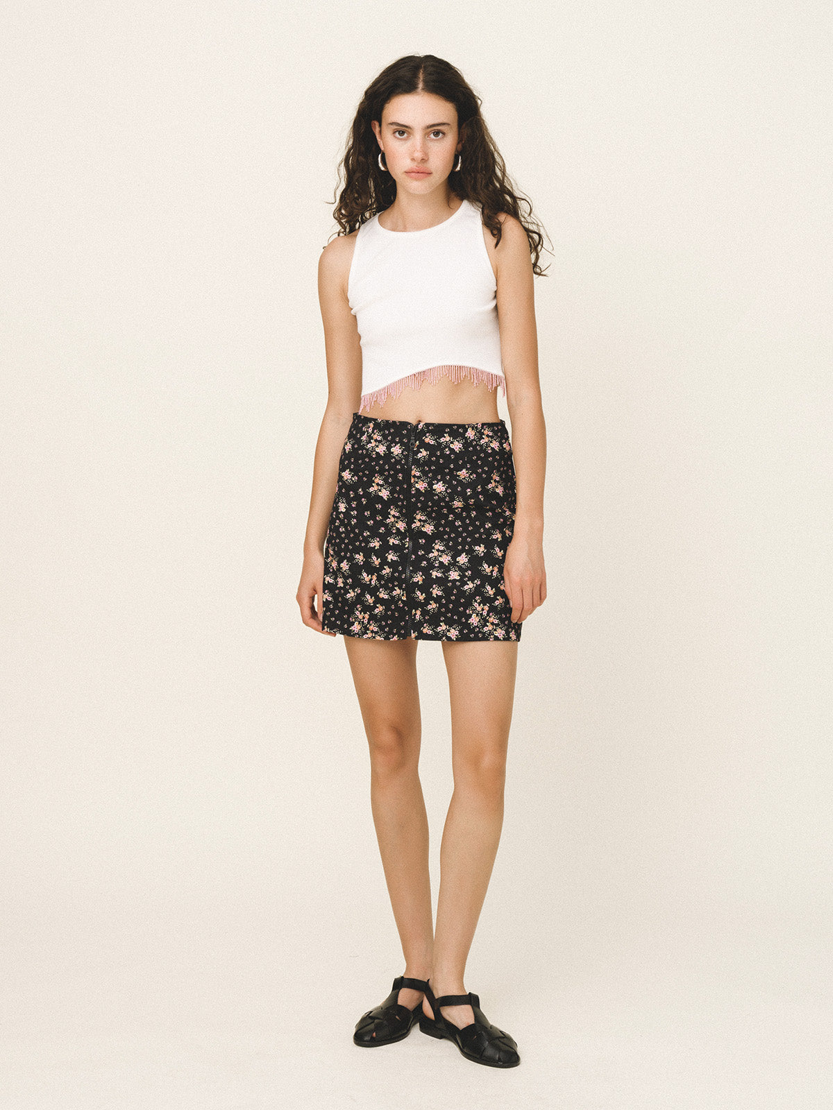Woman wearing a white sleeveless top and black floral skirt on a beige background
