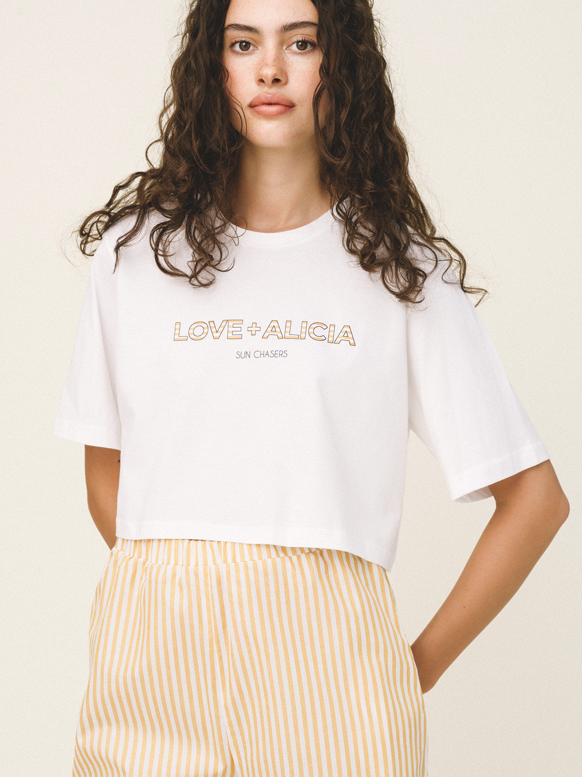 Woman wearing a white t-shirt with 'LOVE ALICIA' text on a beige background