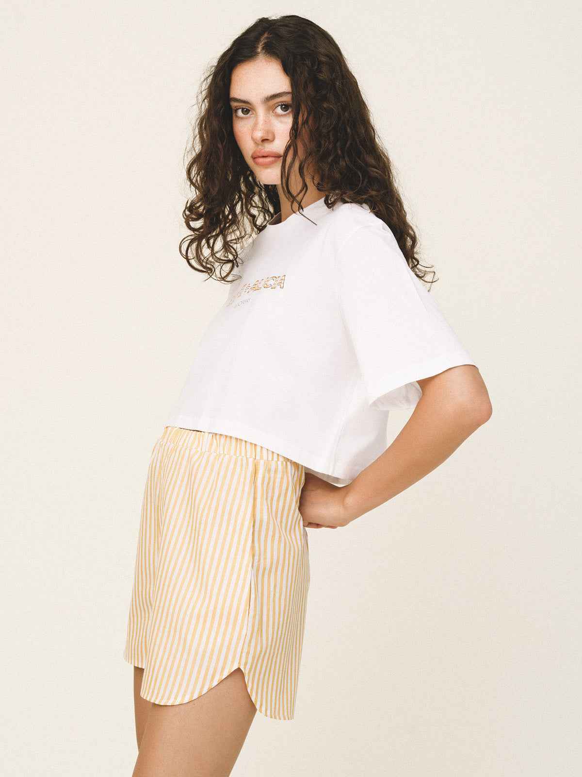 Woman wearing a white oversized t-shirt and yellow striped shorts on a plain background