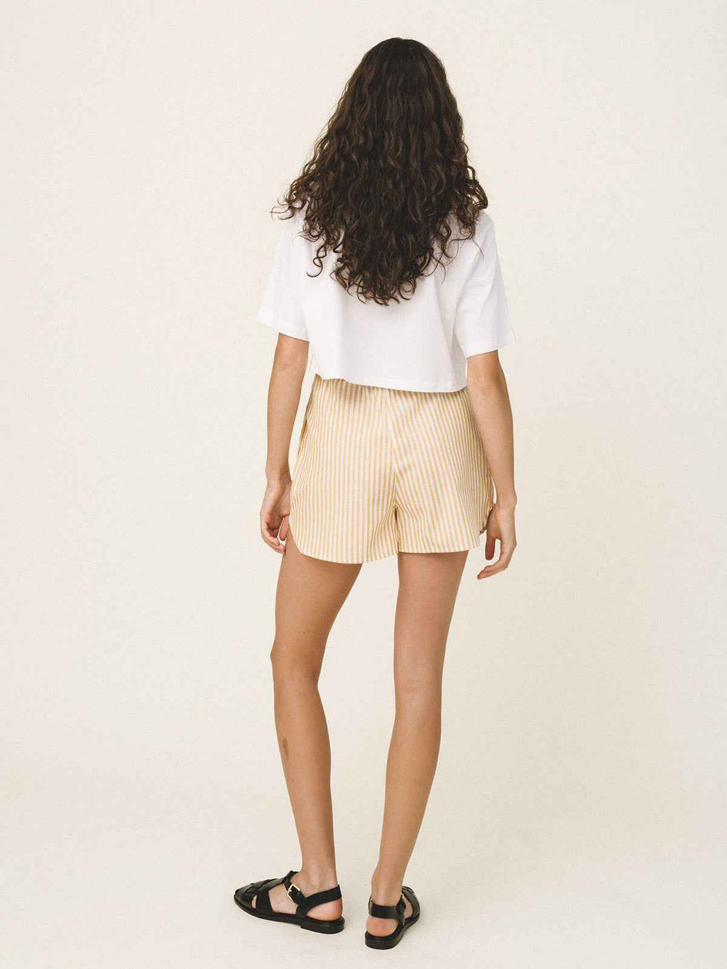 Woman wearing a white top and beige shorts on a plain background