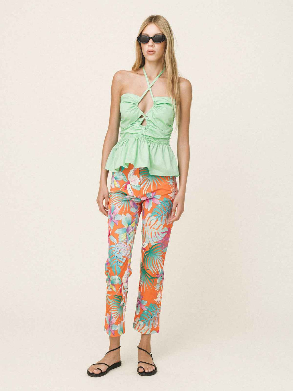 Woman wearing a light green top and colorful floral pants on a white background