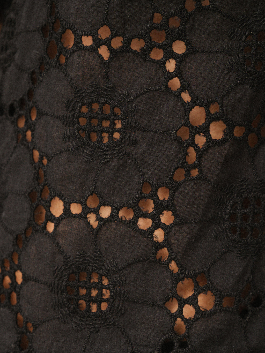 Close-up of a black floral lace fabric with openwork circular and oval cutouts, showing a sheer mesh backing through the holes.