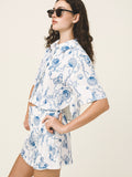 Woman wearing a white outfit with blue sea-themed pattern on a plain background