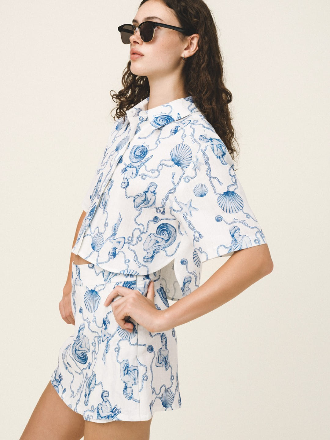 Woman wearing a white outfit with blue sea-themed pattern on a plain background