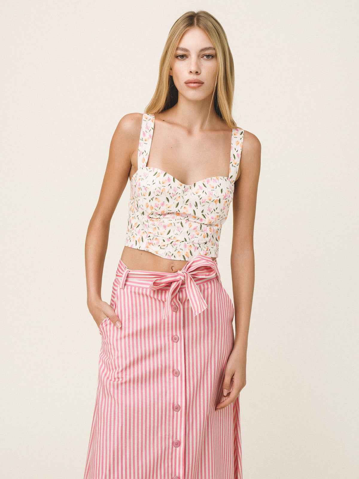 Woman wearing a floral top and pink striped skirt on a plain background