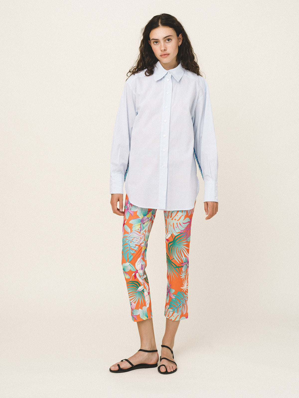 Woman wearing a light blue shirt and colorful floral pants on a beige background