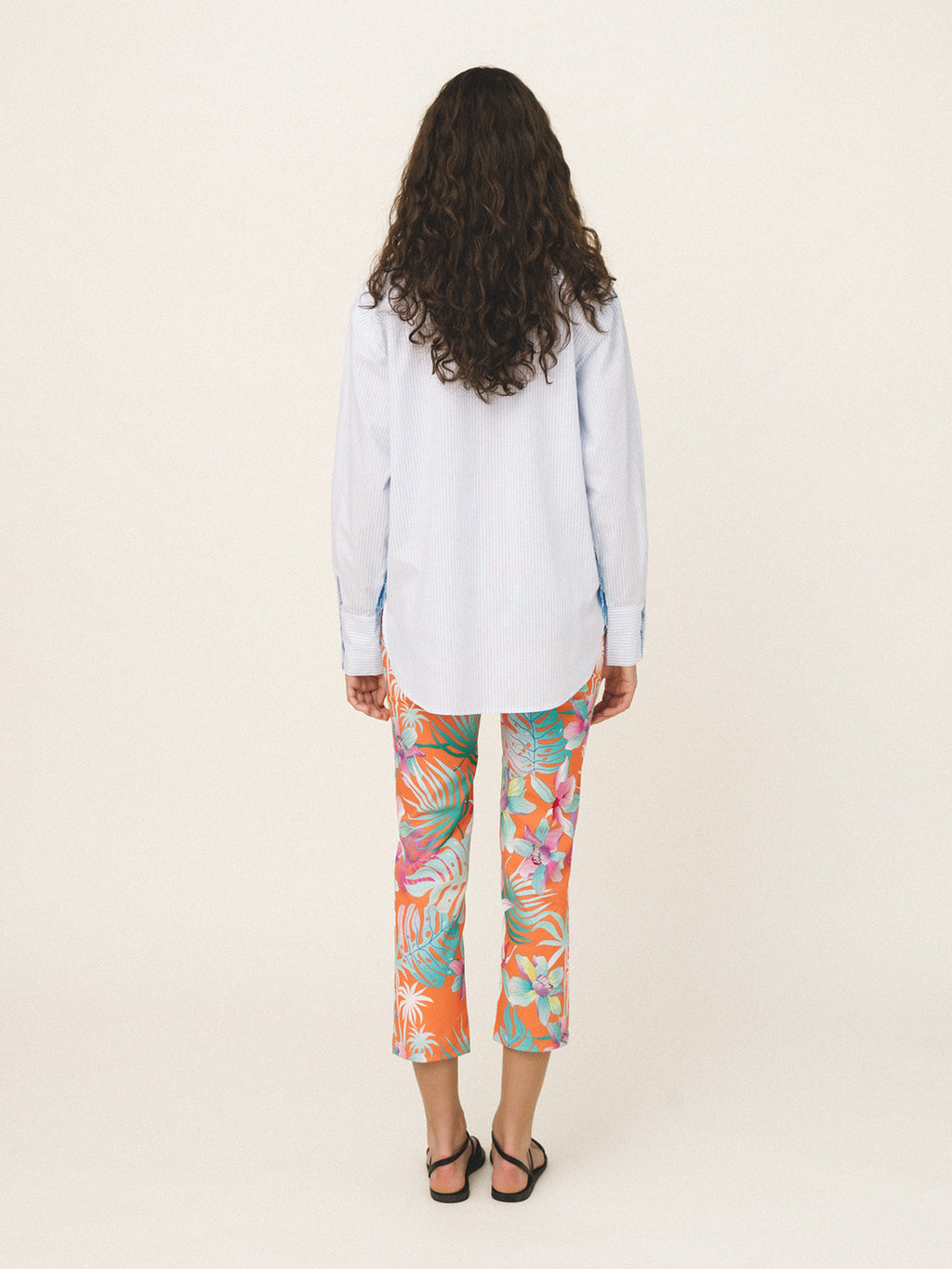 Woman wearing a light blue shirt and colorful floral pants on a white background