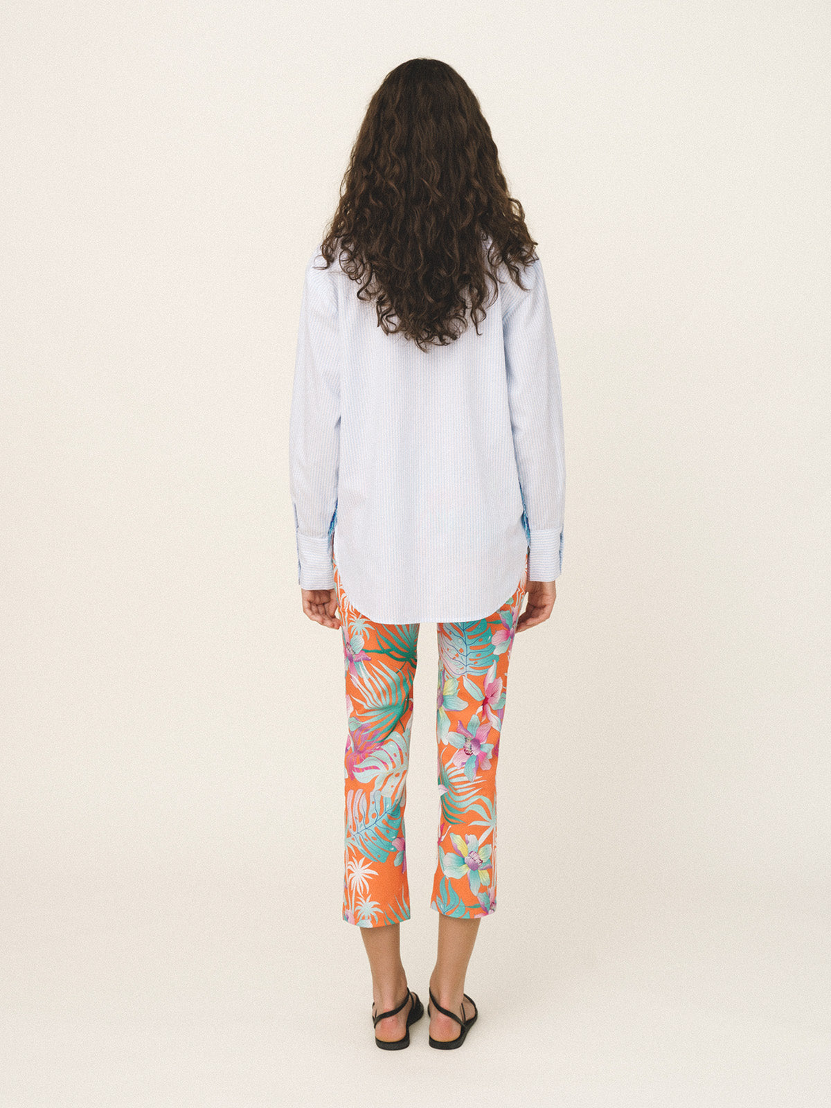 Woman wearing a light blue shirt and colorful floral pants on a white background