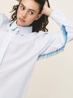 Woman wearing a light blue sweater with fringe details on a beige background
