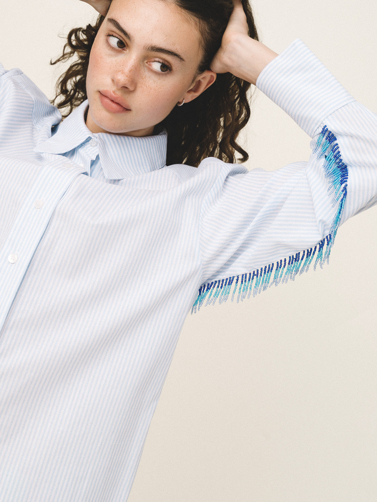 Woman wearing a light blue sweater with fringe details on a beige background