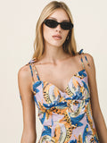 Woman wearing a colorful floral dress with sunglasses on a plain background